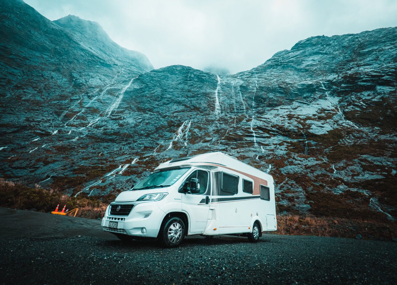 Camper van parked under waterfalls in Milford Sound, New Zealand